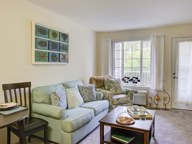 A cozy living room with a sofa, armchair, and a coffee table near a large window.