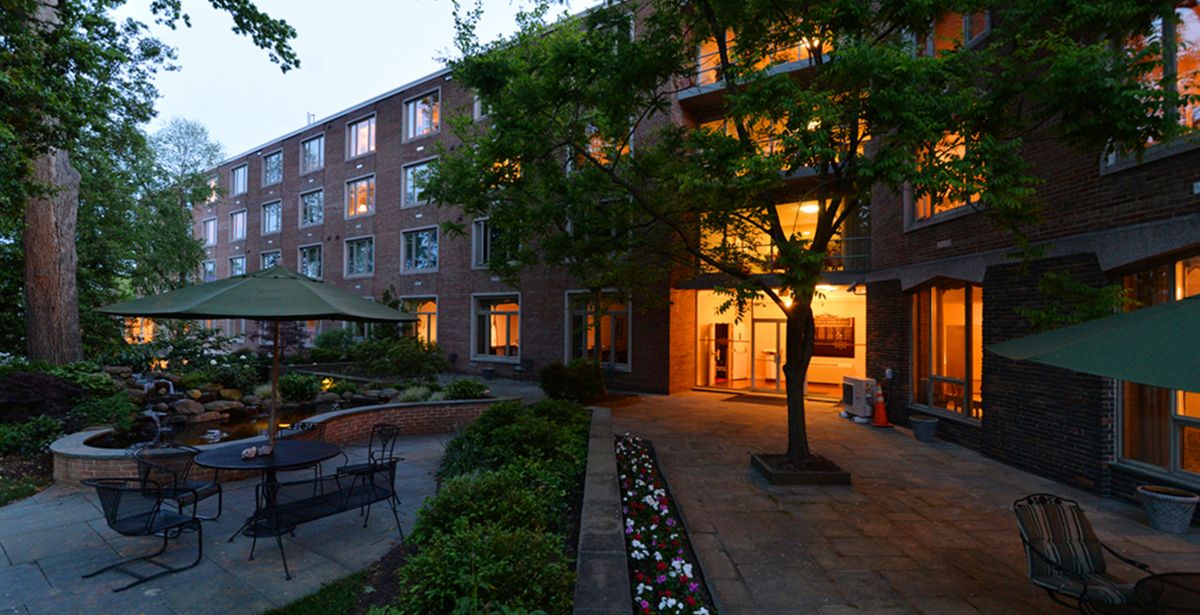 A well-lit apartment building with a brick exterior surrounded by trees and neatly maintained landscaping during the evening.
