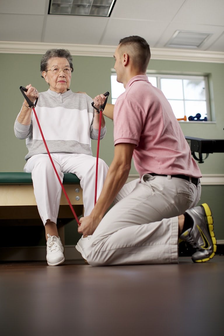 An elderly person receiving guidance from a therapist during a resistance band exercise session.