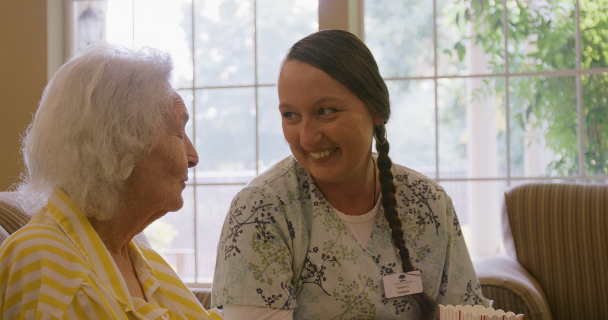 A caregiver smiling while interacting with an elderly person.