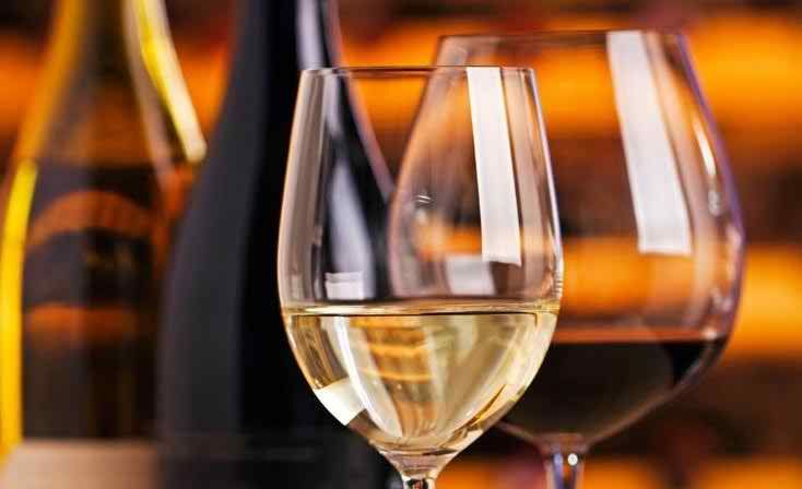 A glass of white wine is elegantly displayed against a blurred background of bottles.