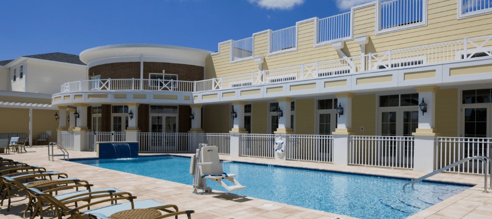 A serene hotel swimming pool area with balconies and lounge chairs under a clear blue sky.