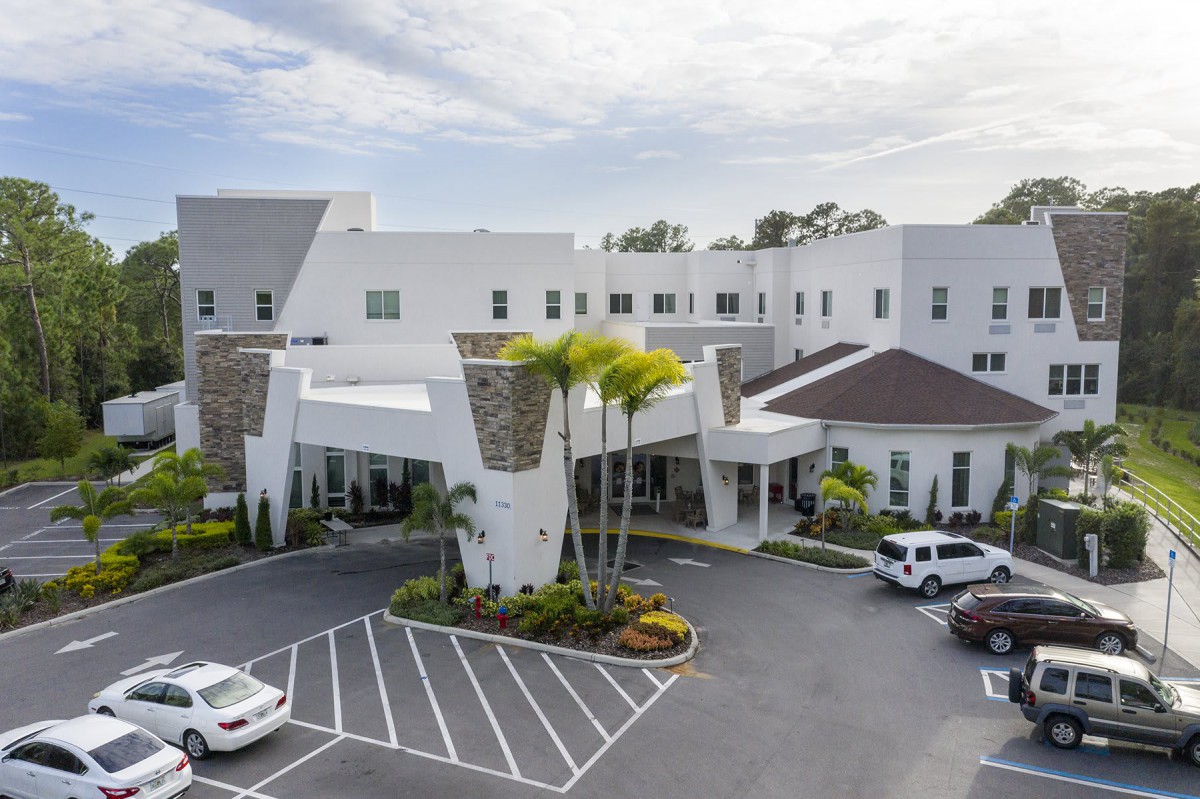 A modern building with a landscaped entrance and adjacent parking lot.