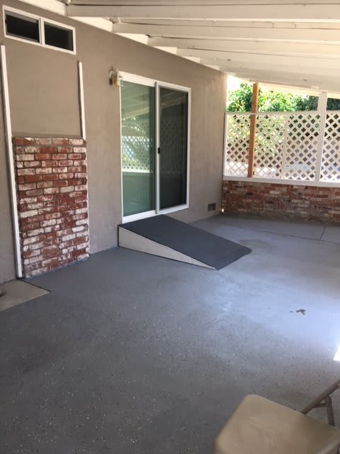 A covered patio area with a ramp leading to sliding glass doors.