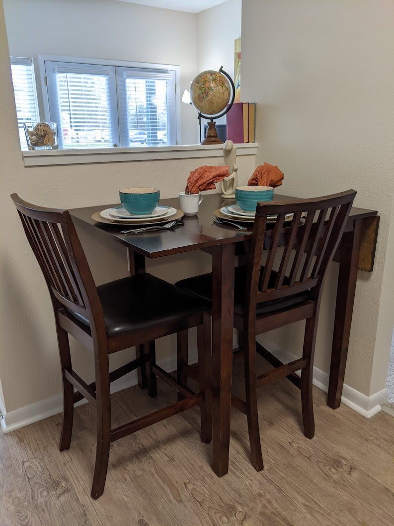 A cozy dining nook with a small set table and two chairs, accented by a globe and natural light from the window.