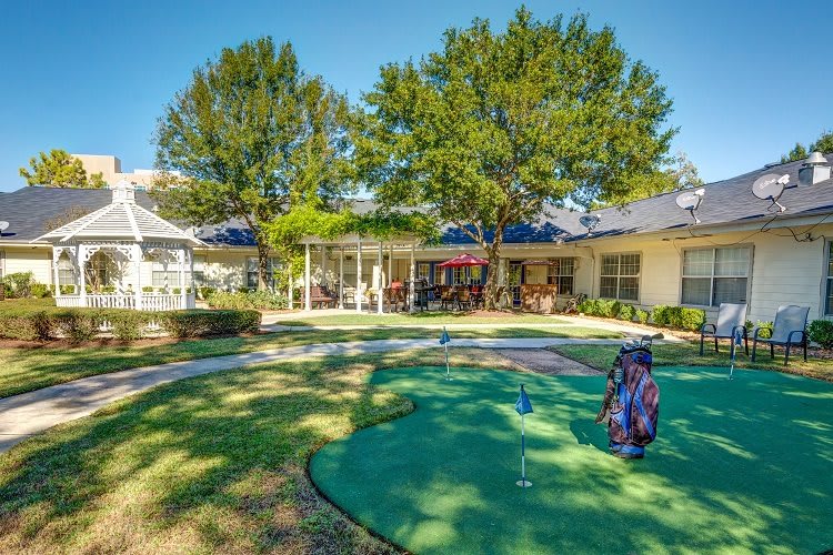 A backyard view of a house with a small putting green and outdoor seating area, surrounded by trees.