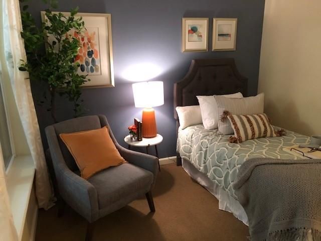 A cozy bedroom features a comfortable armchair, a neatly made bed, and warm lighting from a bedside lamp.