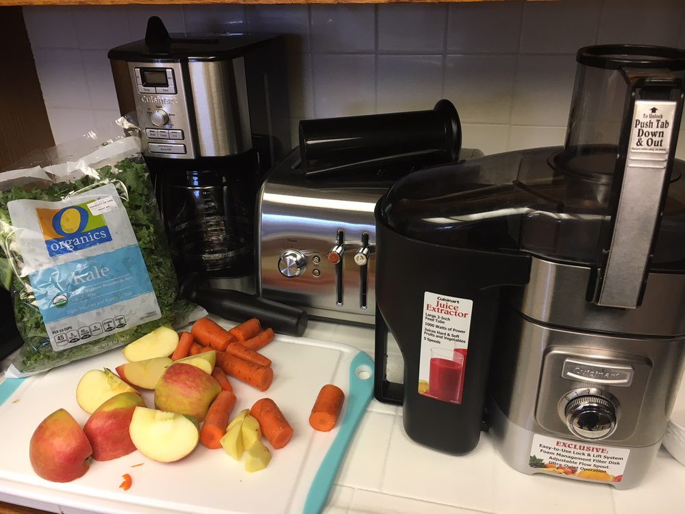 A kitchen counter with a juicer, toaster, and coffee maker alongside chopped fruits and vegetables.