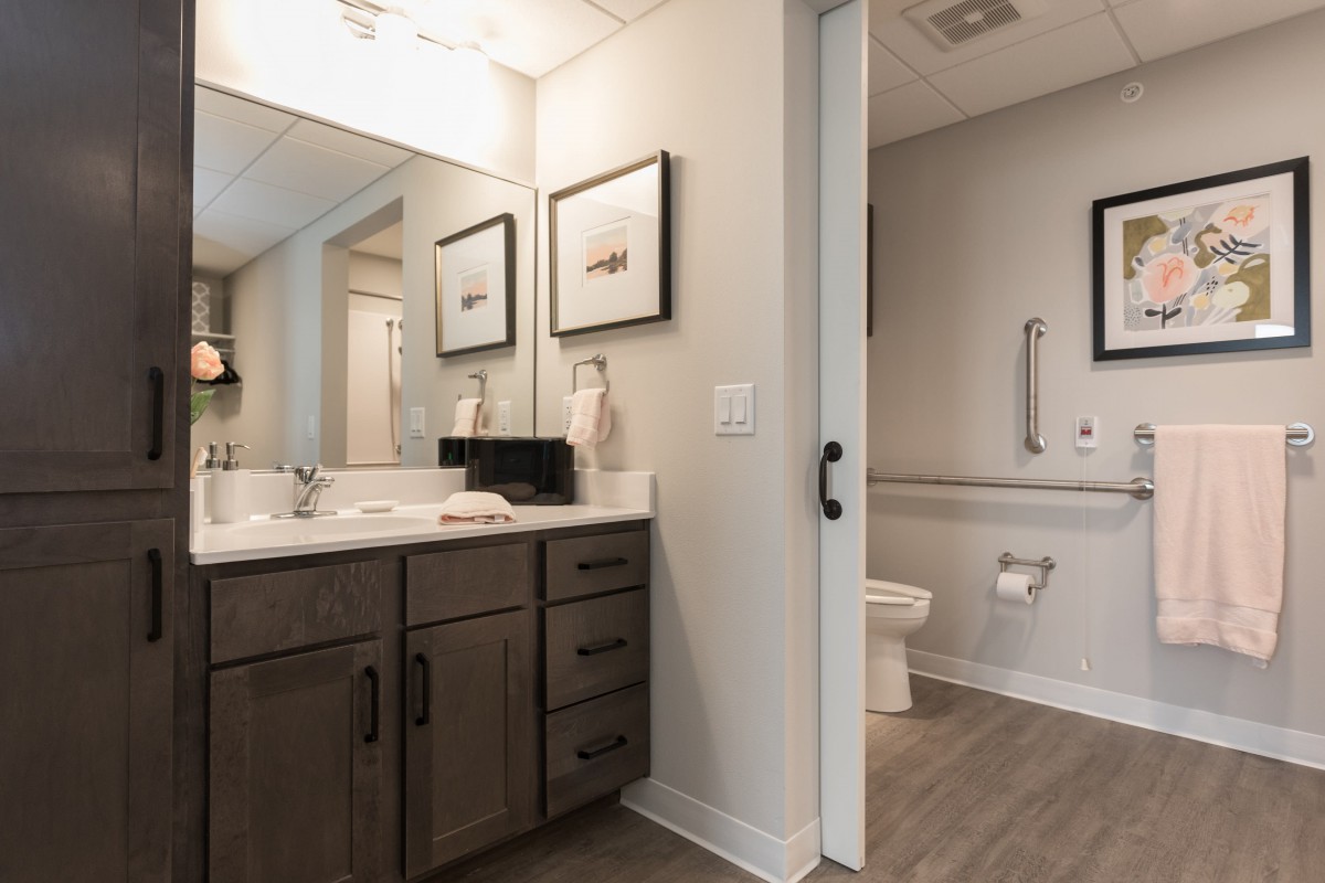 A modern bathroom with a vanity, mirror, and toilet, featuring sleek decor and lighting.