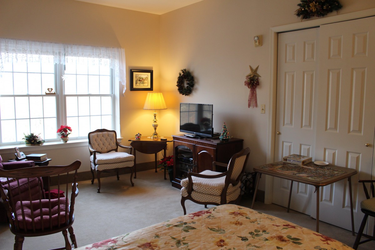 A cozy living room with classic furniture, a television, and soft lighting from a lamp by the window.