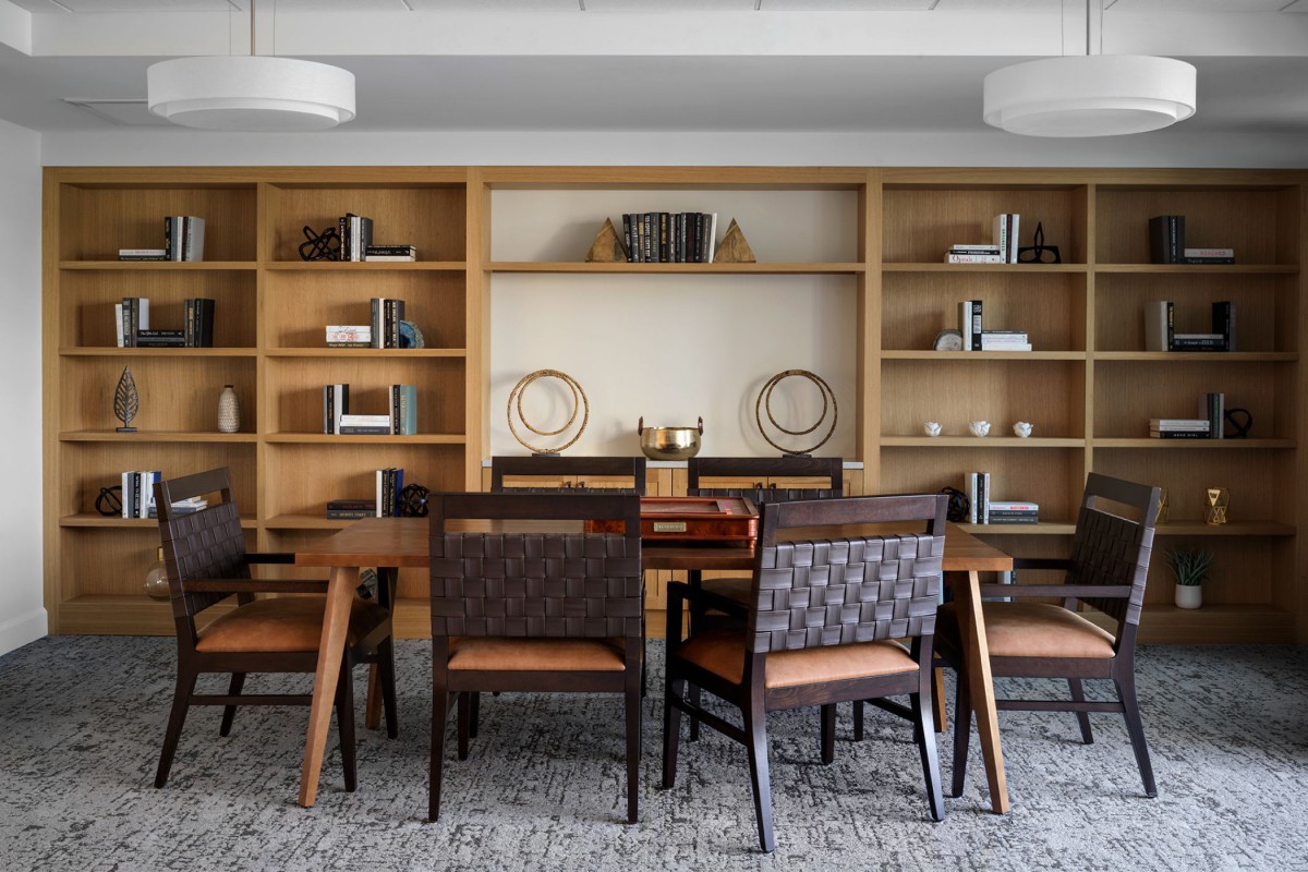 A modern dining room with a wooden table, upholstered chairs, and built-in shelving.
