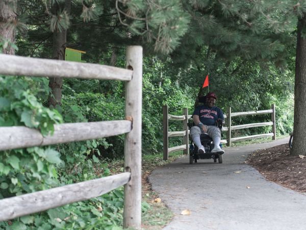 A person in a motorized wheelchair traveling along a wooded path.