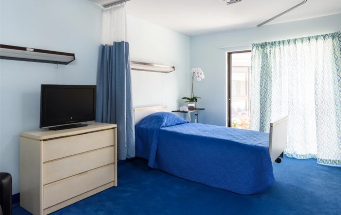 A hospital room with a single bed, television, and blue decor.