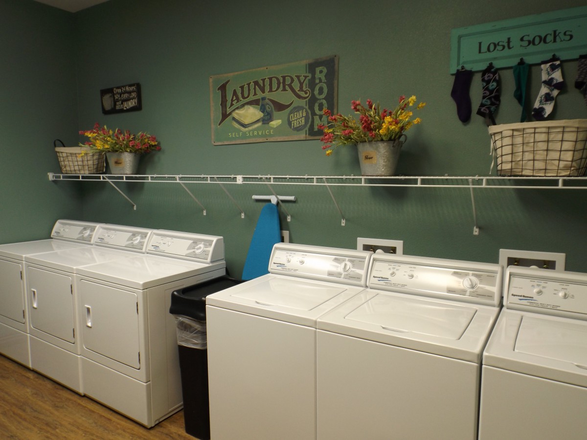 A neatly organized laundry room with washing machines and dryers, decorated with wall signs and floral arrangements.