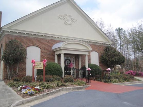 A brick building with a decorative entrance adorned with a wreath, surrounded by well-maintained landscaping and a red carpet leading to the door.