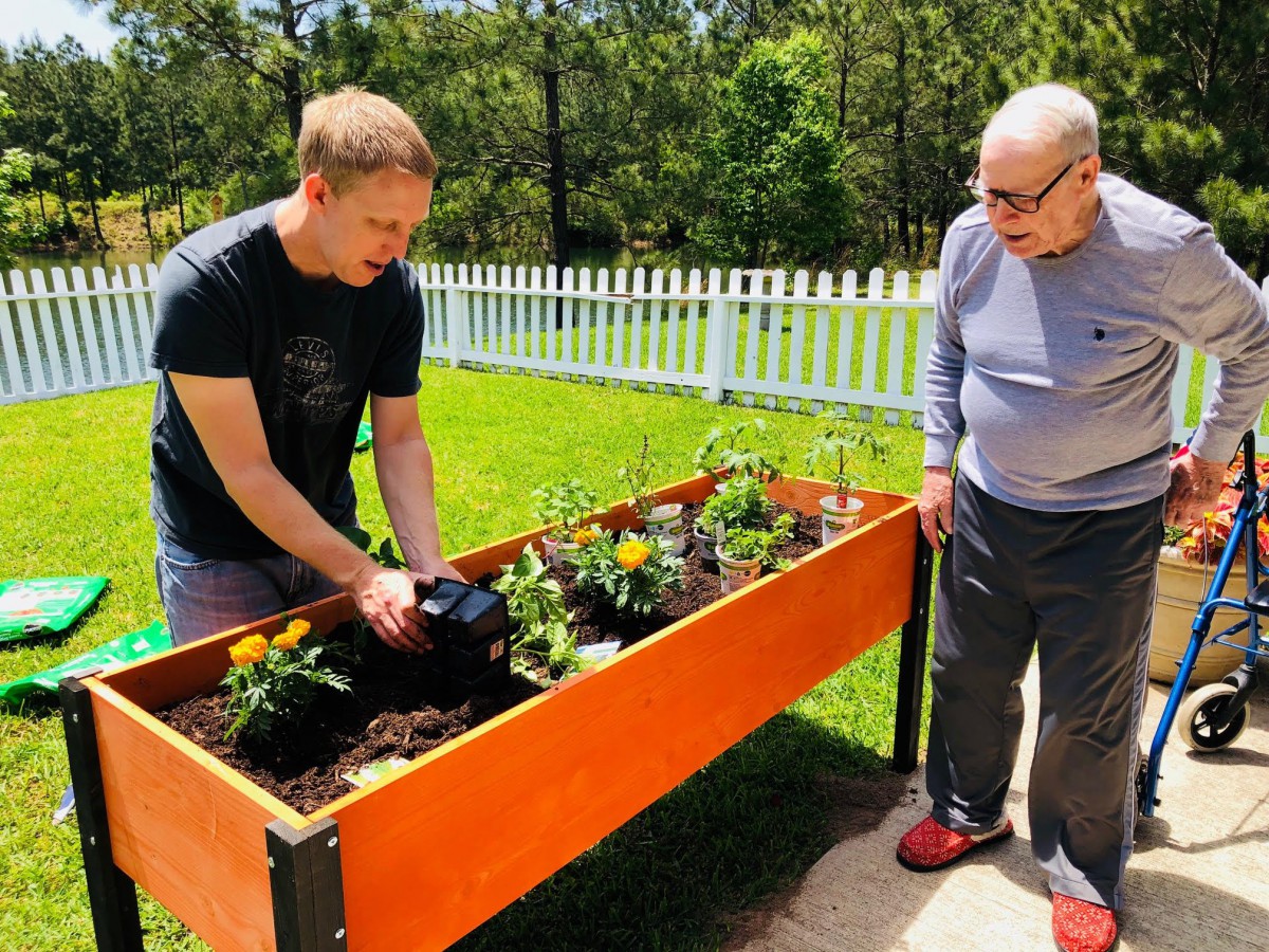 Two people tending to a raised garden bed on a sunny day.