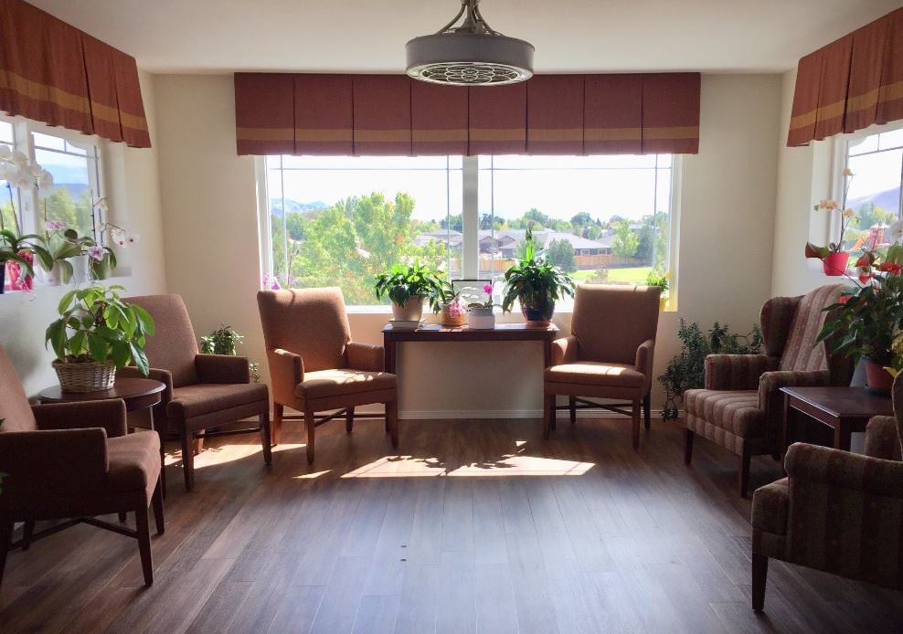 A cozy sitting area with comfortable chairs, decorative plants, and abundant natural light pouring through a large window.