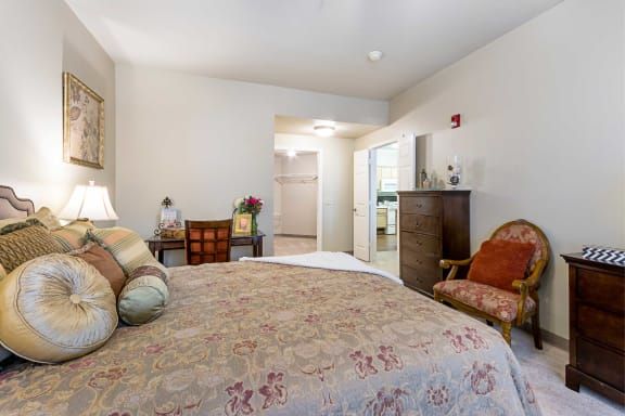 A cozy bedroom with a large bed, wooden dresser, and upholstered chair.