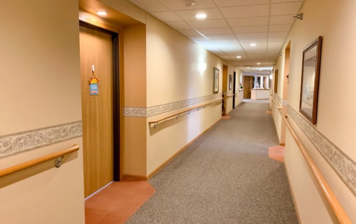 A well-lit hospital corridor with doors and carpeted floor.