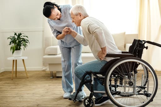 A nurse assisting an elderly man in a wheelchair at home, providing support and care.
