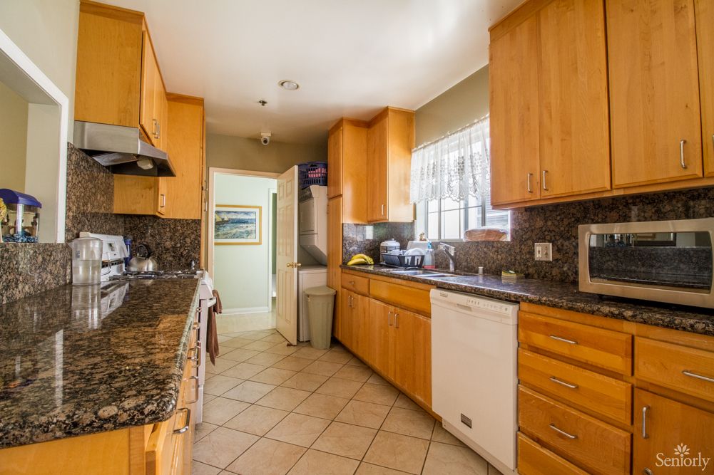 A modern kitchen with wooden cabinets and granite countertops features appliances and a tiled floor.