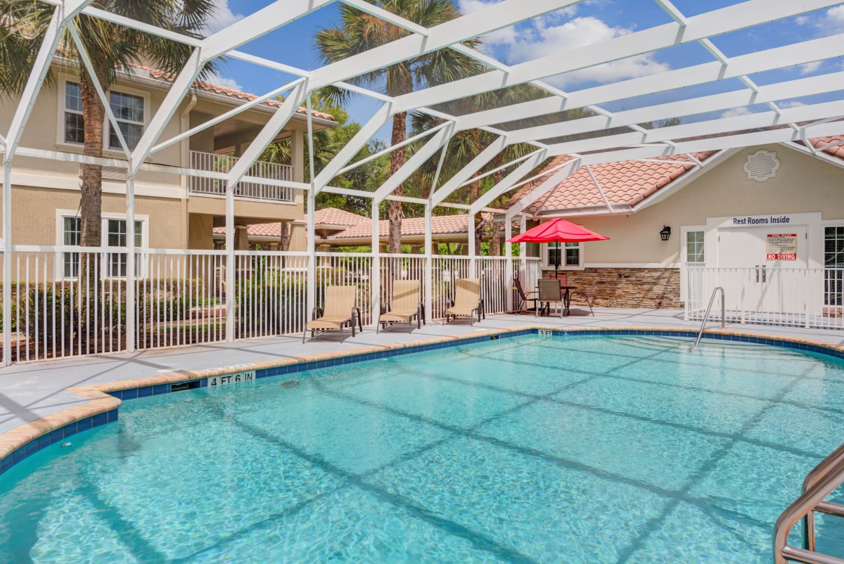 A backyard swimming pool with a protective enclosure, patio furniture, and an umbrella.
