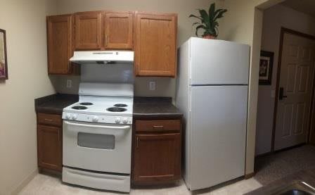 A small kitchen area featuring a stove, refrigerator, and wooden cabinets.