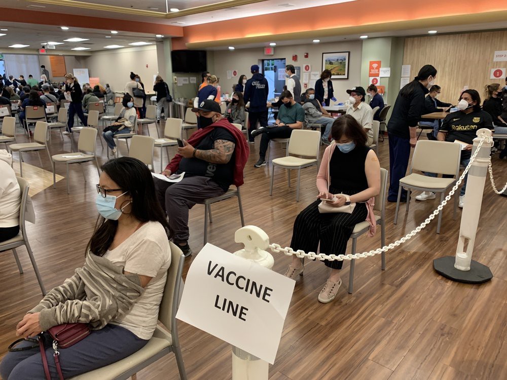 People seated in a waiting area for COVID-19 vaccinations, wearing masks and maintaining social distance.