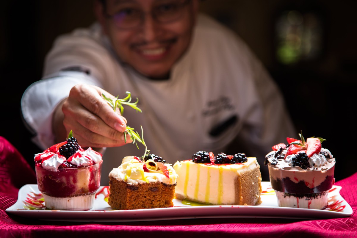 A chef garnishing a selection of beautifully presented desserts with fresh herbs.
