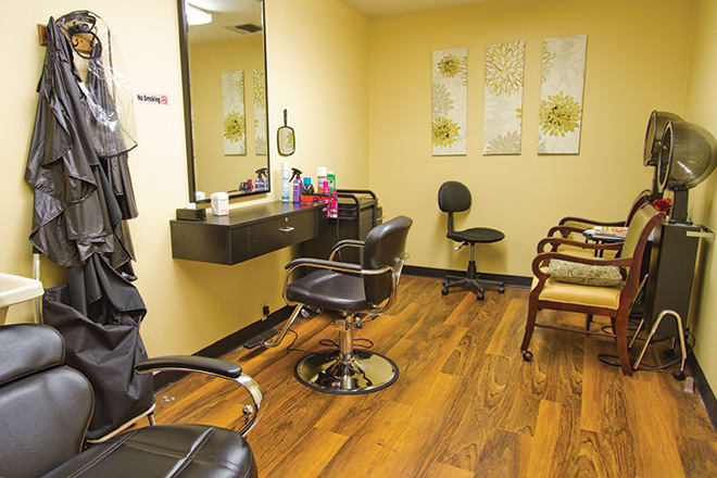 A cozy hair salon interior with styling chairs and a mirror, featuring wooden flooring and salon equipment.