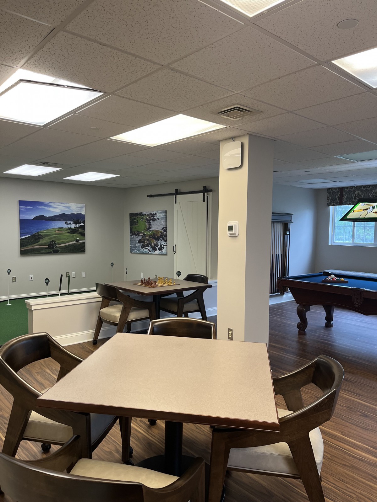 A well-lit recreation room featuring a pool table, tables, and chairs for leisure activities.