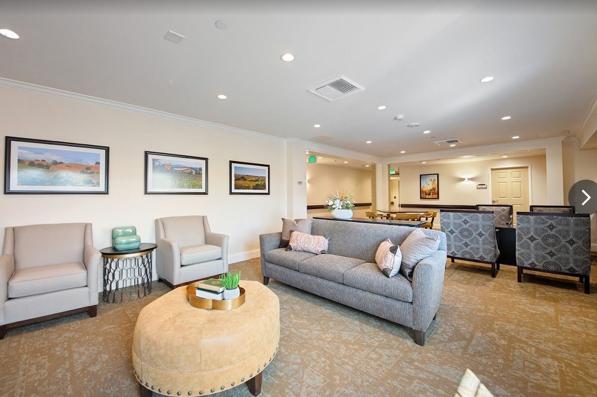 A modern living room with a cozy gray sofa, an armchair, and a round coffee table, decorated with artwork and ambient lighting.