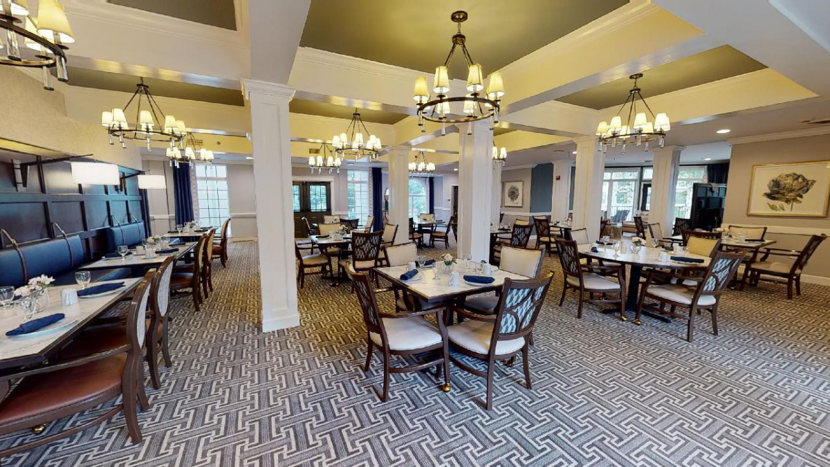 A spacious dining room with elegant decor, featuring multiple tables and chairs under decorative chandeliers.