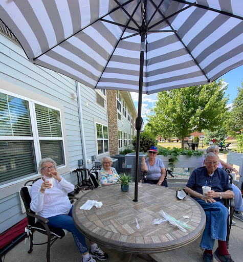 A group of seniors enjoying a sunny day outdoors under an umbrella, sharing laughter and conversation.