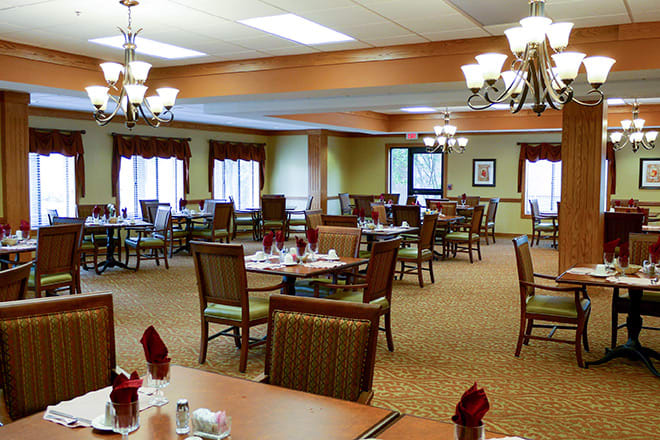A spacious dining room with neatly arranged tables and chairs, well-lit by elegant chandeliers.