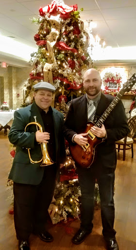 Two musicians posing together in front of a beautifully decorated Christmas tree.