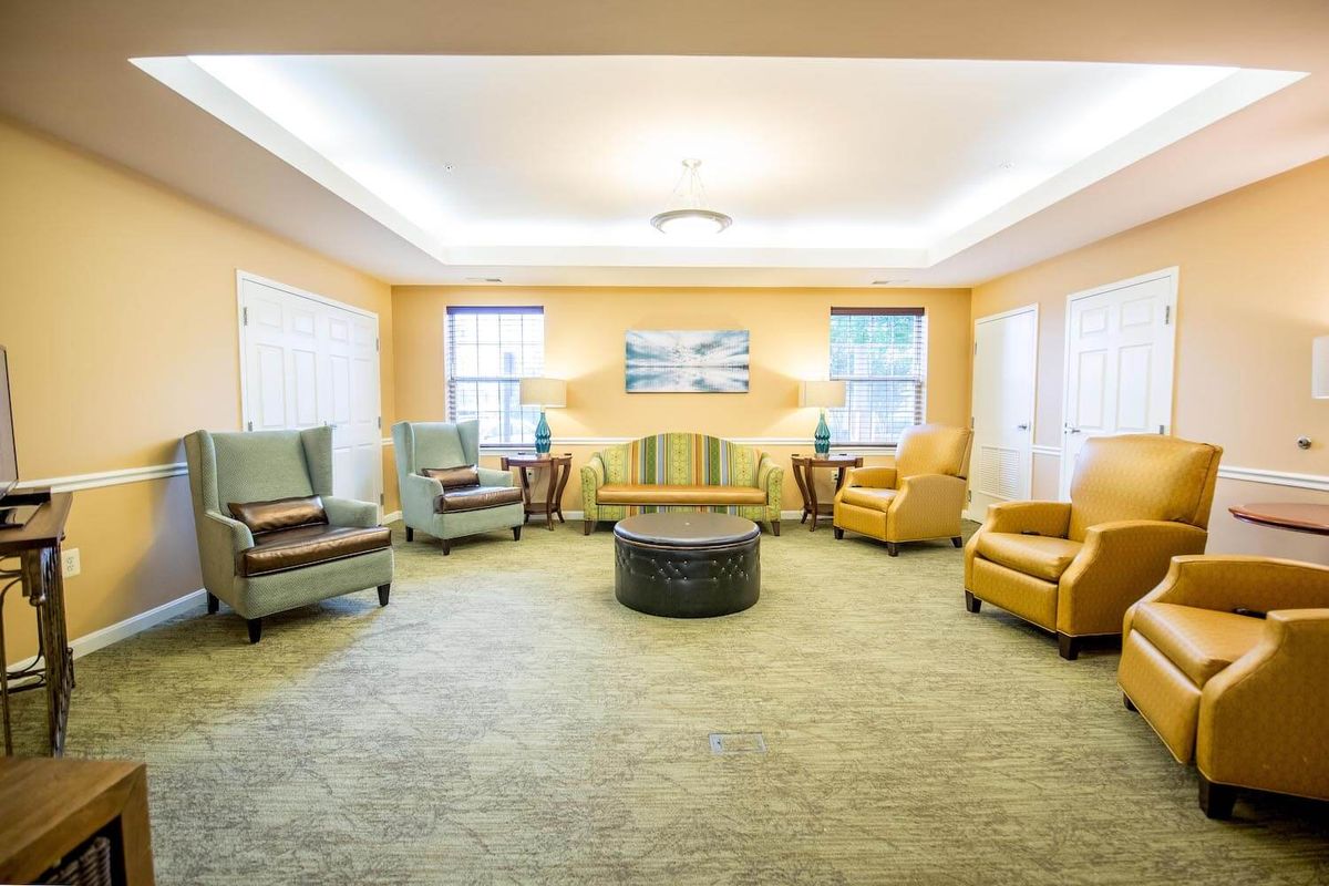 A cozy living room with comfortable chairs and a central coffee table, illuminated by bright lighting.