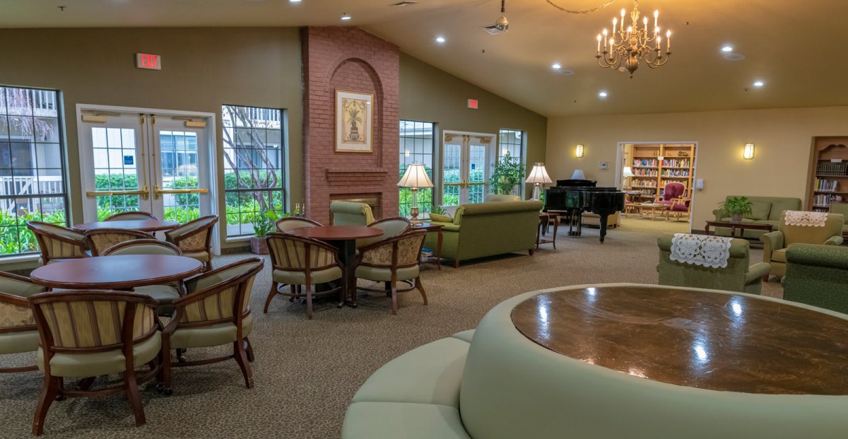 A cozy living room with comfortable seating, a piano, and large windows providing natural light.