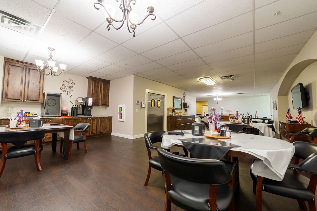 A cozy dining area with neatly arranged tables and chairs, illuminated by chandeliers.