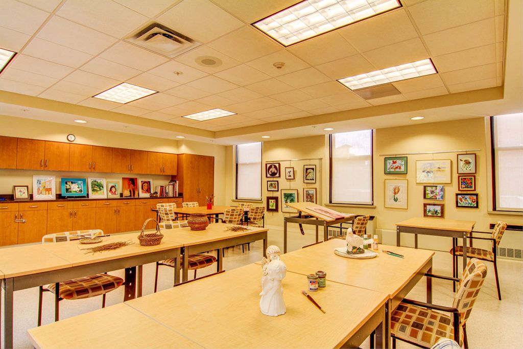 A well-lit art studio with tables and chairs, featuring art supplies and drawings displayed on the walls.