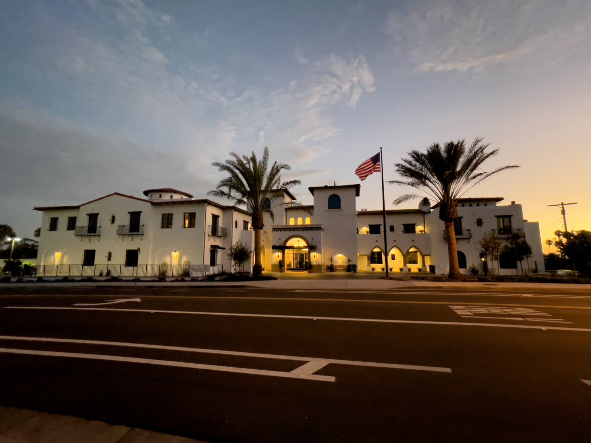 A well-lit building with palm trees and an American flag at dusk.