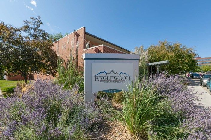 A sign for Englewood surrounded by lush greenery and foliage, with a brick building in the background under a clear blue sky.