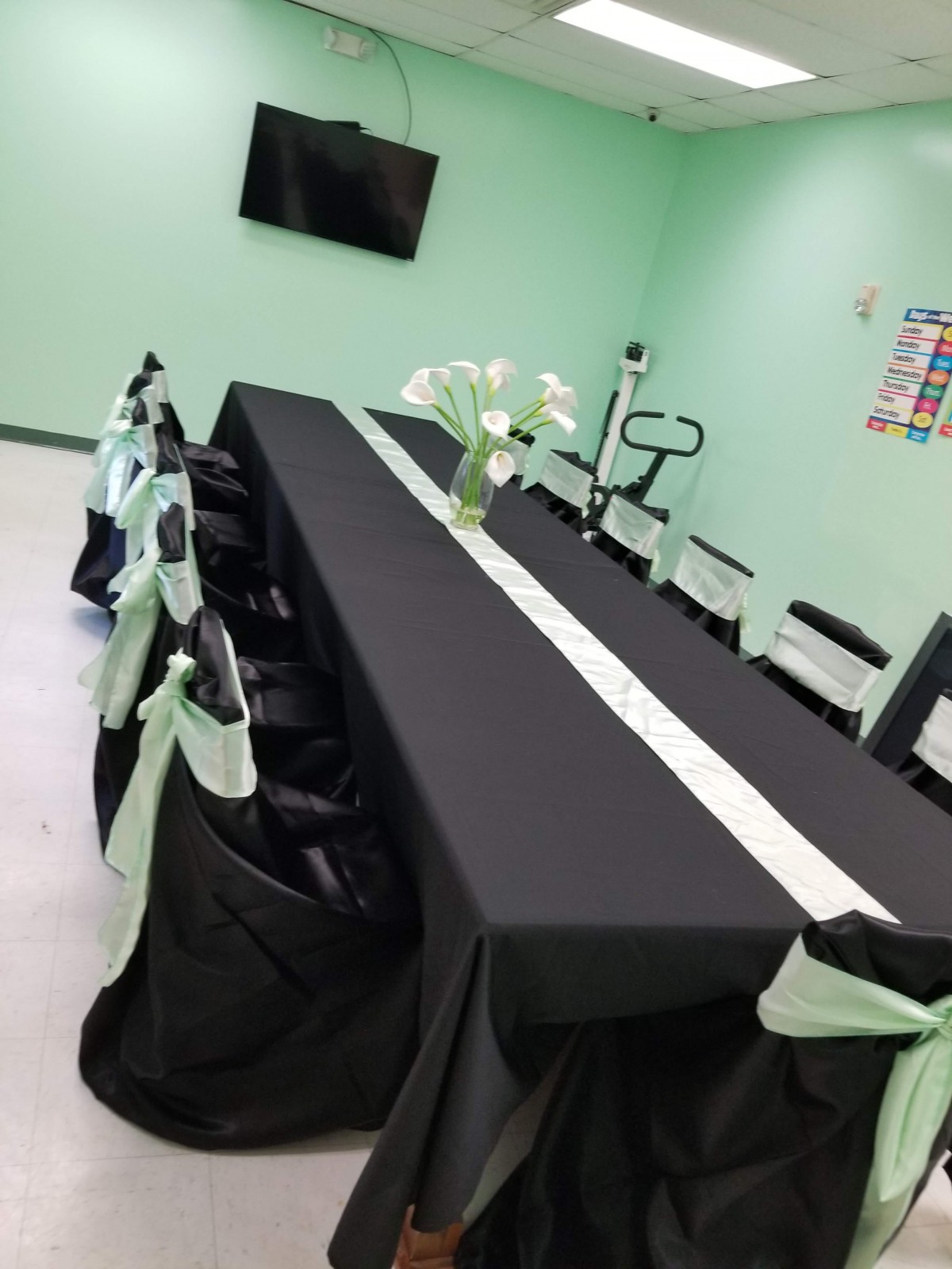 A conference room with a long meeting table covered in a black tablecloth and decorated with green accents. Chairs are neatly arranged with matching decor, and a vase of flowers sits at the center of the table.