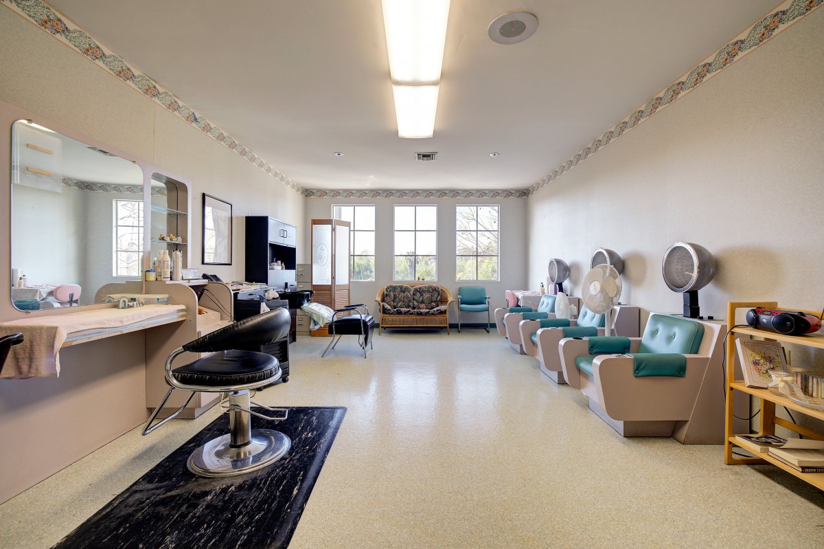 A spacious hair salon with styling chairs, mirrors, and hair dryers lined up along the wall.
