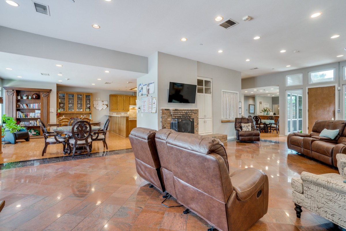 A spacious living room with an open floor plan connecting to the kitchen and dining area, featuring comfortable seating, a fireplace, and a mounted television.