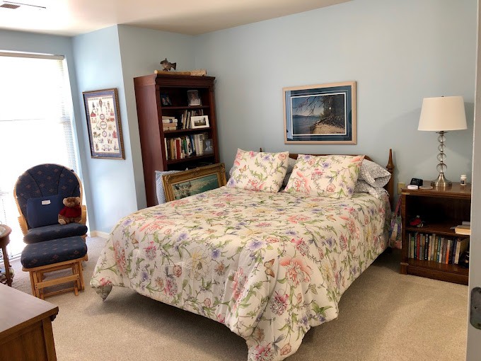 A cozy bedroom featuring a bed with floral bedding, a bookshelf, and wall decorations.