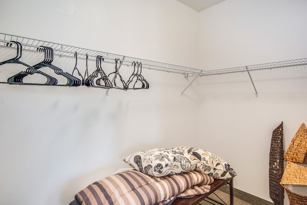 A spacious closet with wire shelves and empty hangers, featuring a few pillows on the lower shelf.