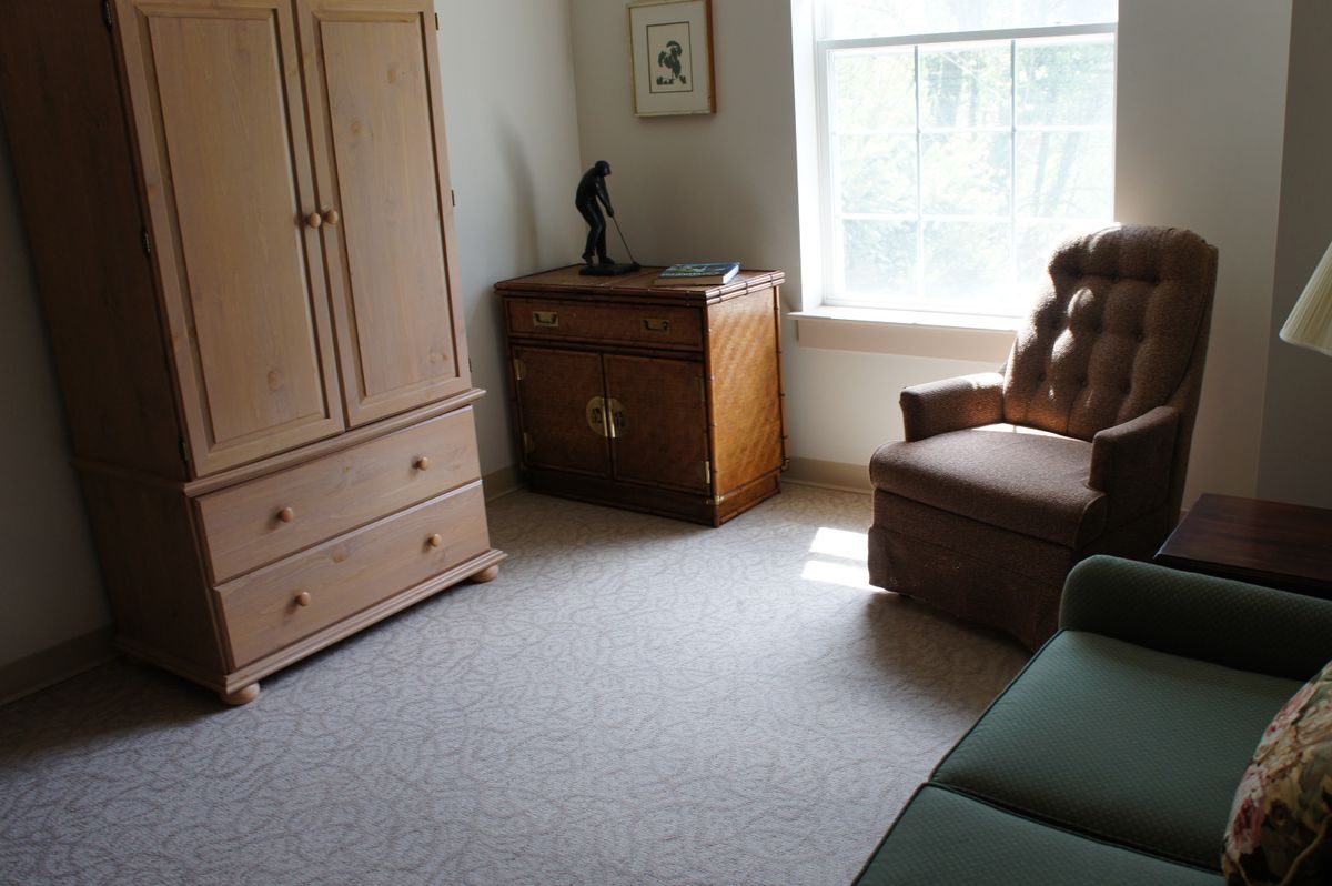 A cozy room with a chair, cabinet, and window letting in natural light.
