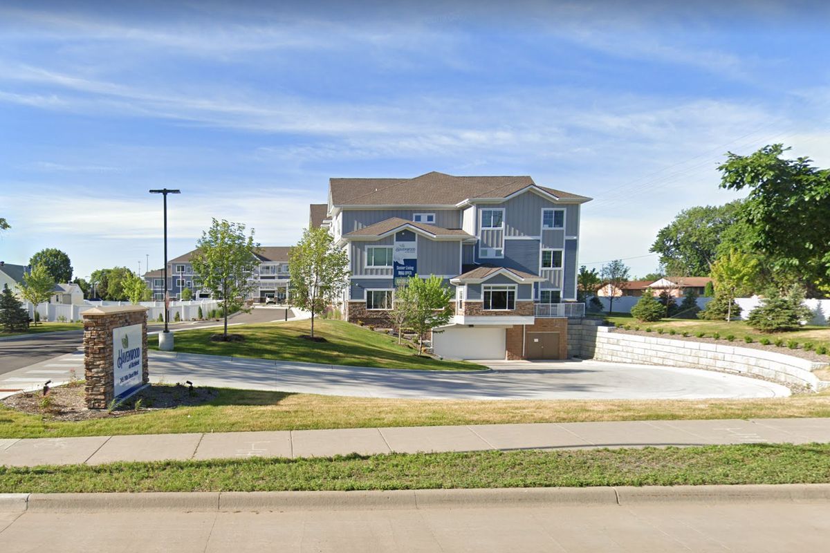 A suburban residential house with a driveway and surrounding greenery on a sunny day.