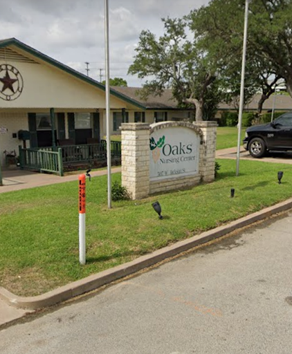A view of a building with a sign in a residential area, featuring some greenery and a parked vehicle.